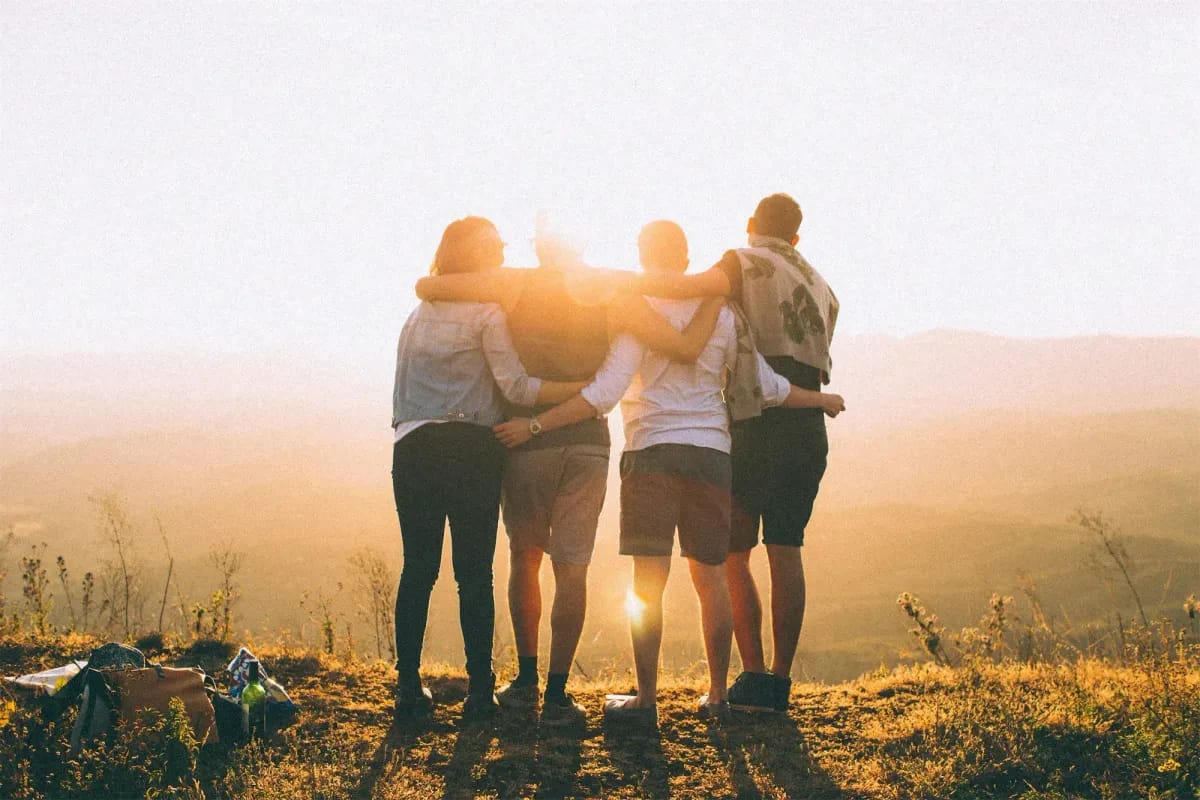 Four friends huddle together at sunset in grassy field, backlit by golden light